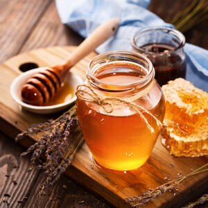 Jar of liquid honey with honeycomb inside and bunch of dry lavender over old wooden table. Dark rustic style, selective focus